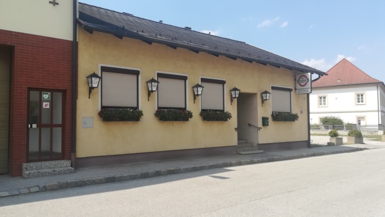 Au&szlig;enansicht eines gelben Gasthauses mit geschlossenen Fensterl&auml;den und Blumenk&auml;sten.