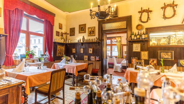 Gemütliches Restaurant mit Holzmöbeln, roten Vorhängen und dekorativen Bildern an den Wänden.