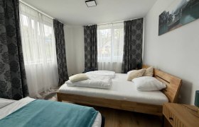 Helles Schlafzimmer mit zwei Betten, Holzboden und gro&szlig;en Fenstern mit Vorh&auml;ngen.