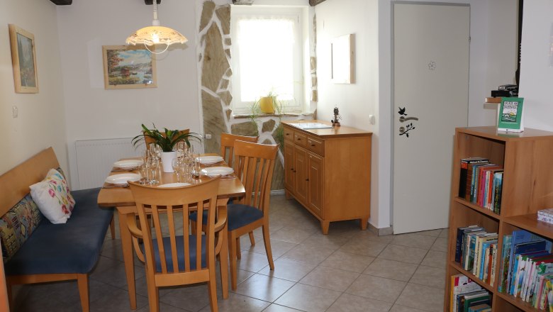 Essbereich mit Holztisch, Stühlen und Bücherregal.