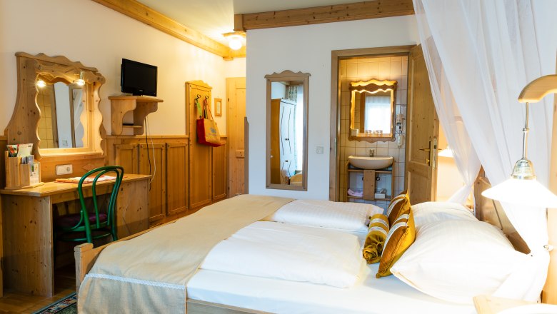 Gemütliches Hotelzimmer mit Doppelbett, Holzmöbeln und kleinem Badezimmer.