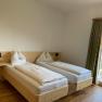 Double room with wooden floor, two single beds, bedside lamps and a balcony with a view of the countryside.
