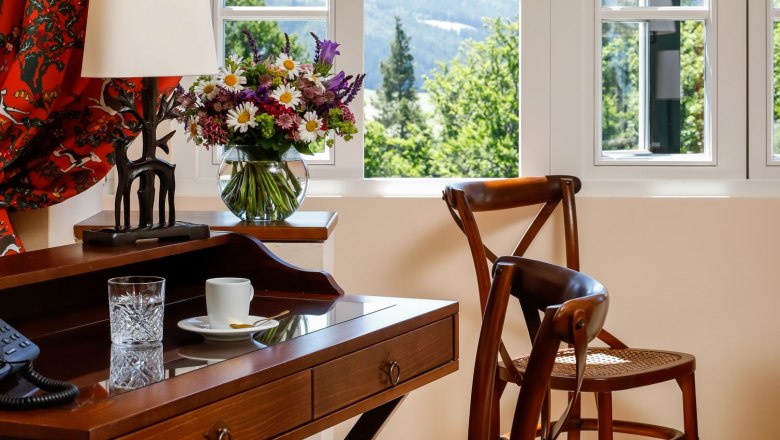 Ein elegantes Zimmer mit Holzm&ouml;beln, einem Schreibtisch, St&uuml;hlen und einem Fenster mit Blick auf eine gr&uuml;ne Landschaft.