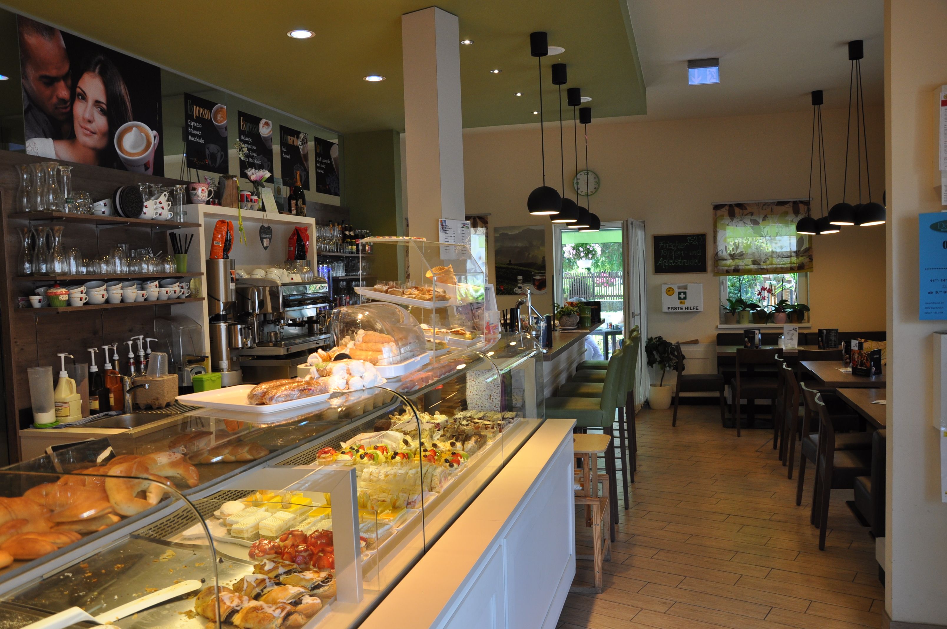 Innenansicht eines Cafés mit Theke voller Gebäck und Sitzbereich.