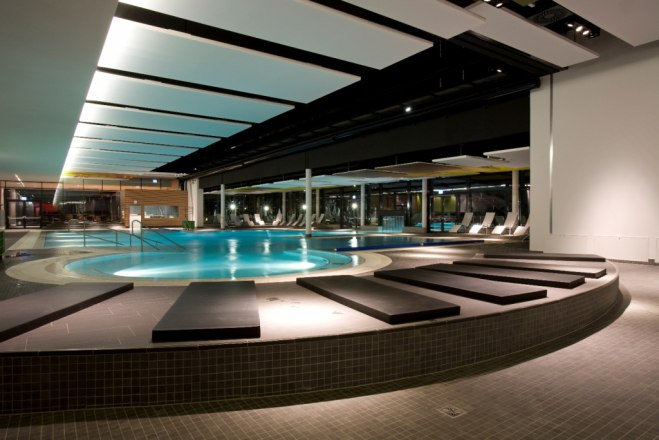 Innenansicht eines modernen Thermenbereichs mit beleuchtetem Pool und Liegestühlen.