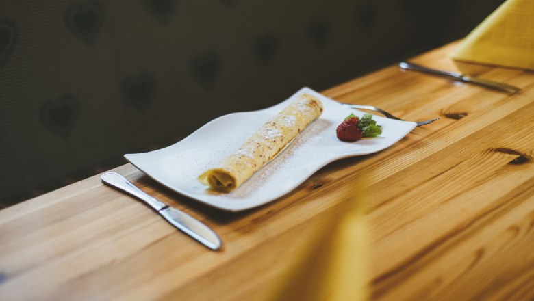 Palacinka na bielom tanieri s jahodami a m&auml;tou, pod&aacute;van&aacute; na drevenom stole.