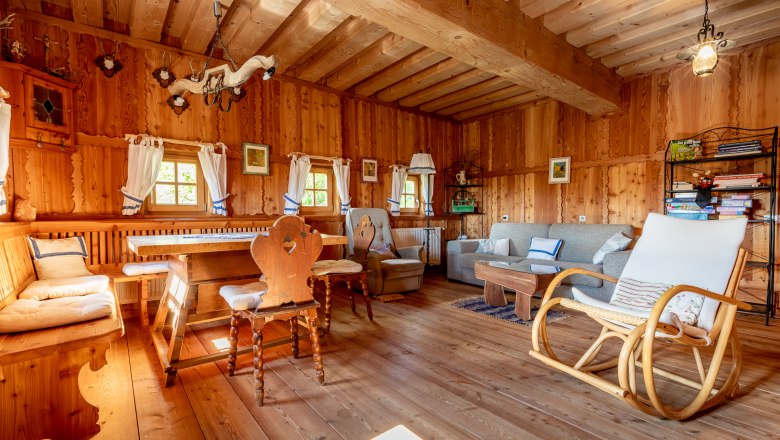 Essbereich mit Holzm&ouml;beln, Schaukelstuhl und Sofa in einem Raum mit Holzvert&auml;felung.