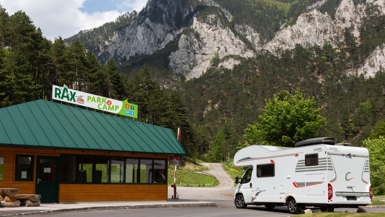 Wohnmobil vor dem Rax Park'n'Camp Gebäude mit Bergkulisse.