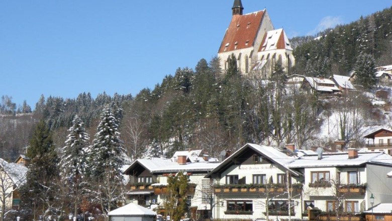 Winterlandschaft mit Kirche und Gasthof im Vordergrund.