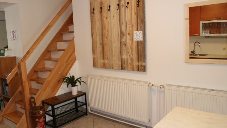 Innenraum mit Holztreppe, Garderobe, Pflanze und Küchenfenster.