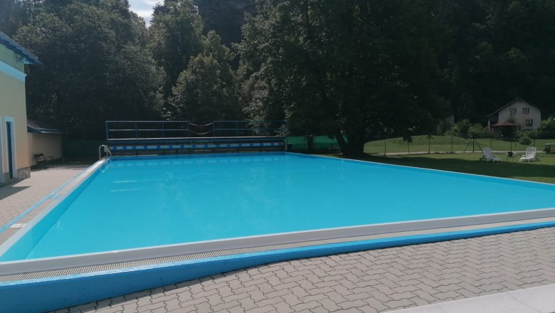 Ein leerer Swimmingpool im Freien, umgeben von Bäumen und einem Gebäude.