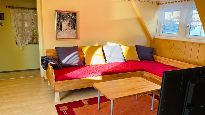 Wohnzimmer mit rotem Sofa, Holztisch und Fernseher.