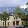 Yellow house in front of a snow-covered mountain and cloudy sky.