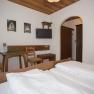 A cozy double room with wooden furniture, a double bed, a small table with two chairs and a TV on the wall.