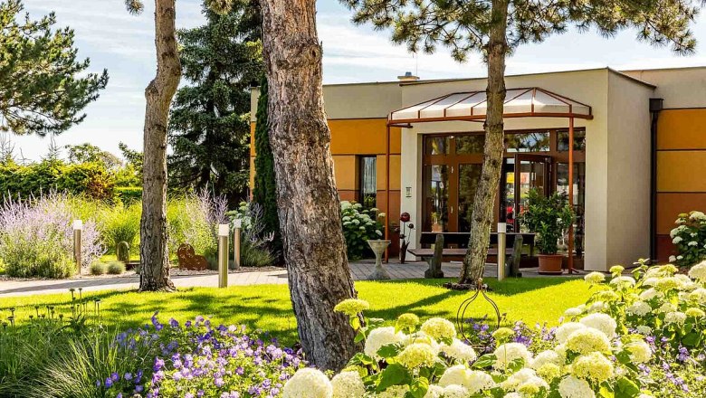 Eingang eines modernen Gebäudes mit Garten und Bäumen.