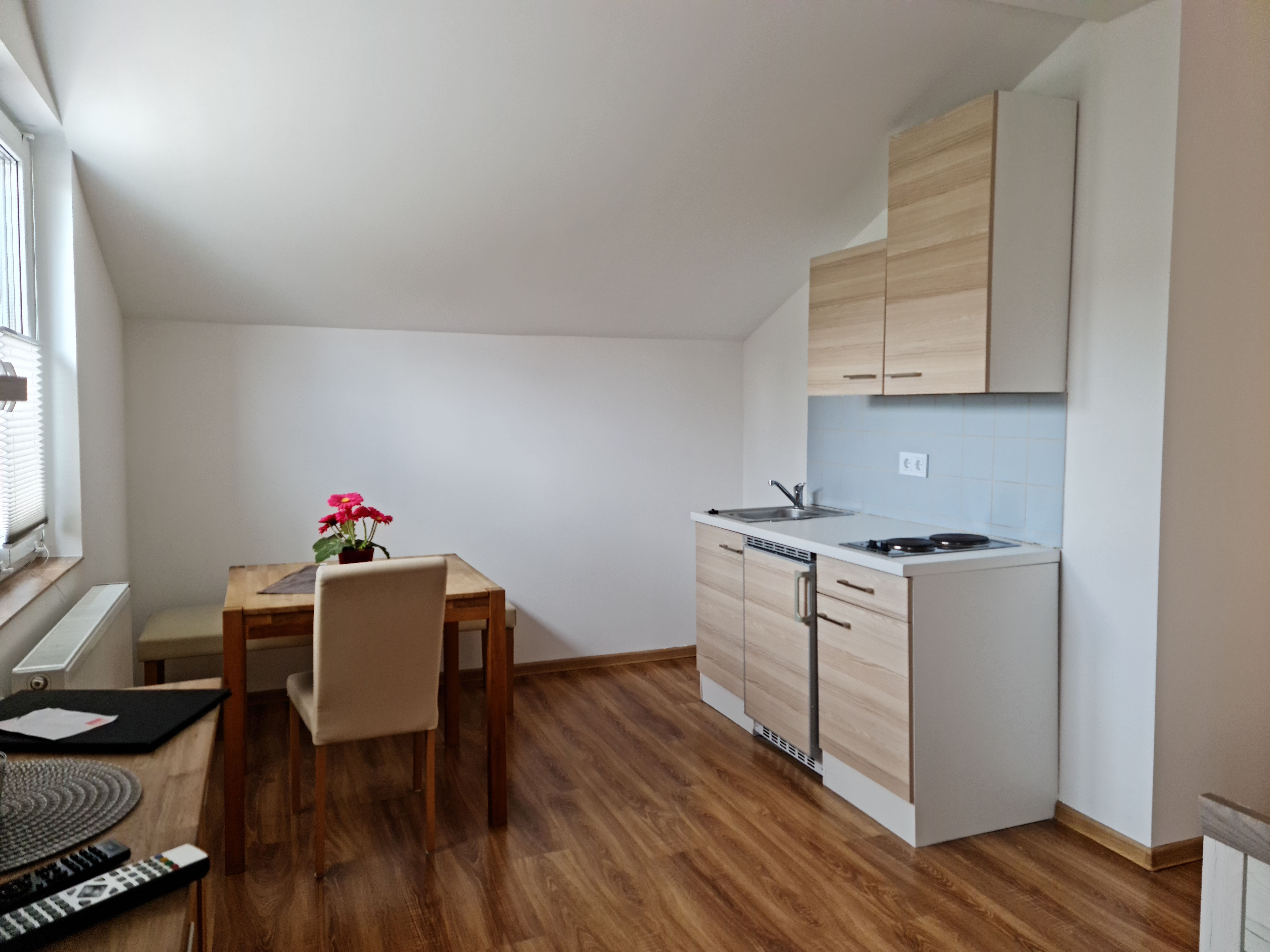 Kleine Küche mit Esstisch und Stuhl in einem hellen Raum mit Dachschräge.