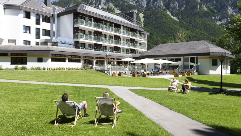 Parkhotel Hirschwang mit Liegestühlen auf einer grünen Wiese und Bergen im Hintergrund.