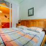 Bedroom with double bed, wooden furniture and view into a living room with orange lighting.