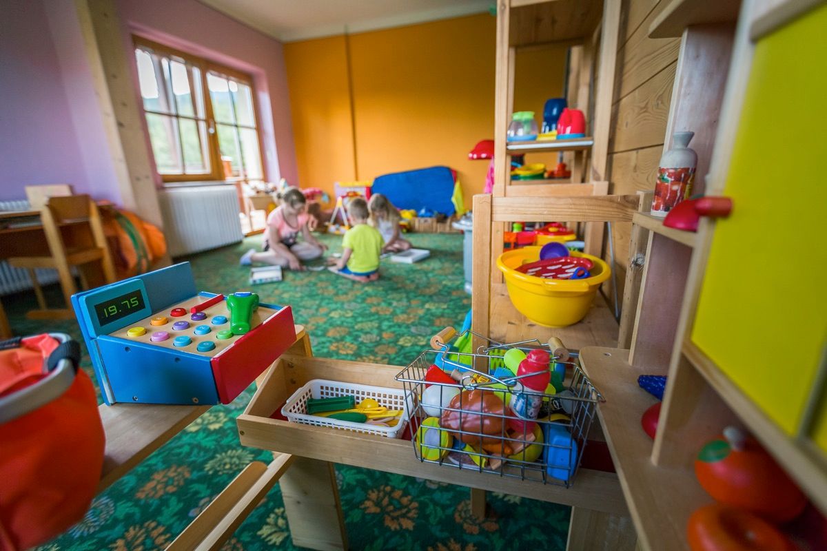 Spielzimmer mit bunten Spielsachen und Kindern im Hintergrund.