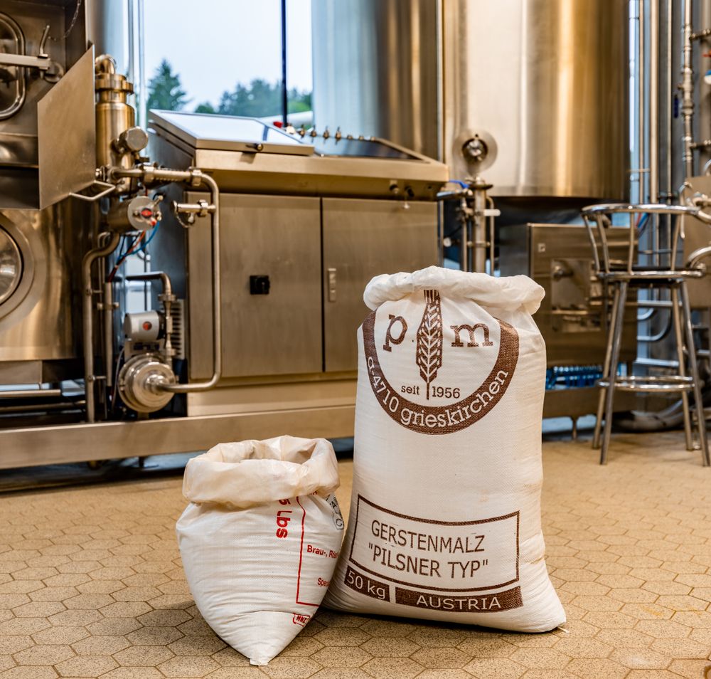 Zwei große Säcke mit Gerstenmalz stehen am Boden der Brauerei Schwarzbräu. Im Hintergrund Braumaschinen aus Edelstahl.