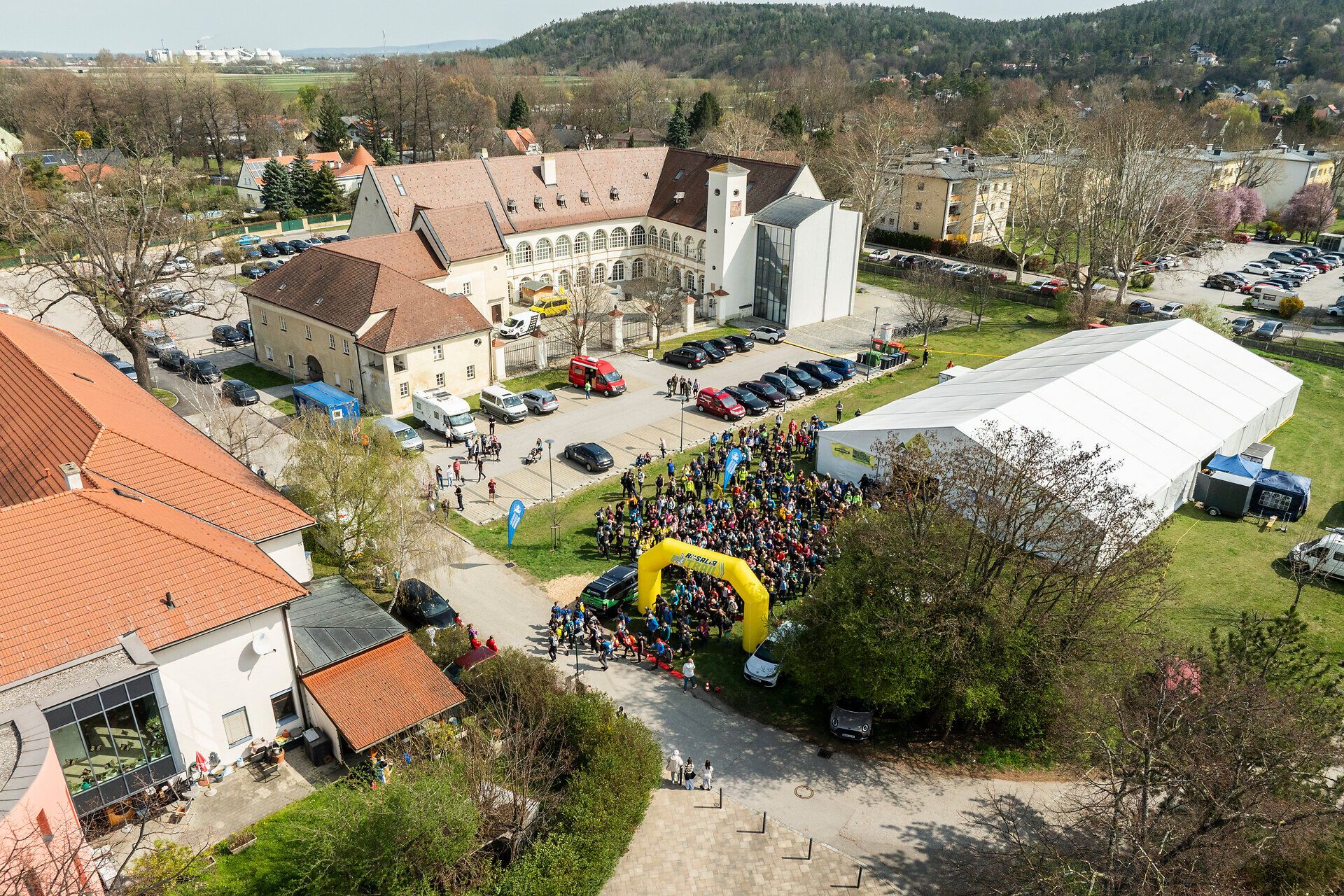 Eine Luftansicht zeigt das Schloss Katzelsdorf bei der „Rosalia Trail Challenge“ mit einem großen Festzelt auf der Wiese und dem Startbogen, umgeben von einer Menschenmenge.