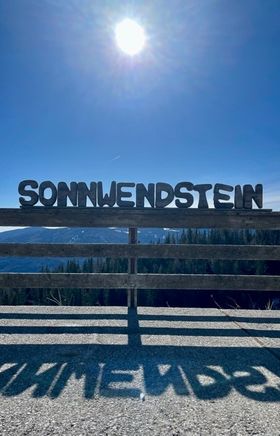 Ausblick auf Sonnenschein und blauenhimmel von der Pollereshütte, davor ein Zaun mit dem Schriftzug "SONNWENDSTEIN"