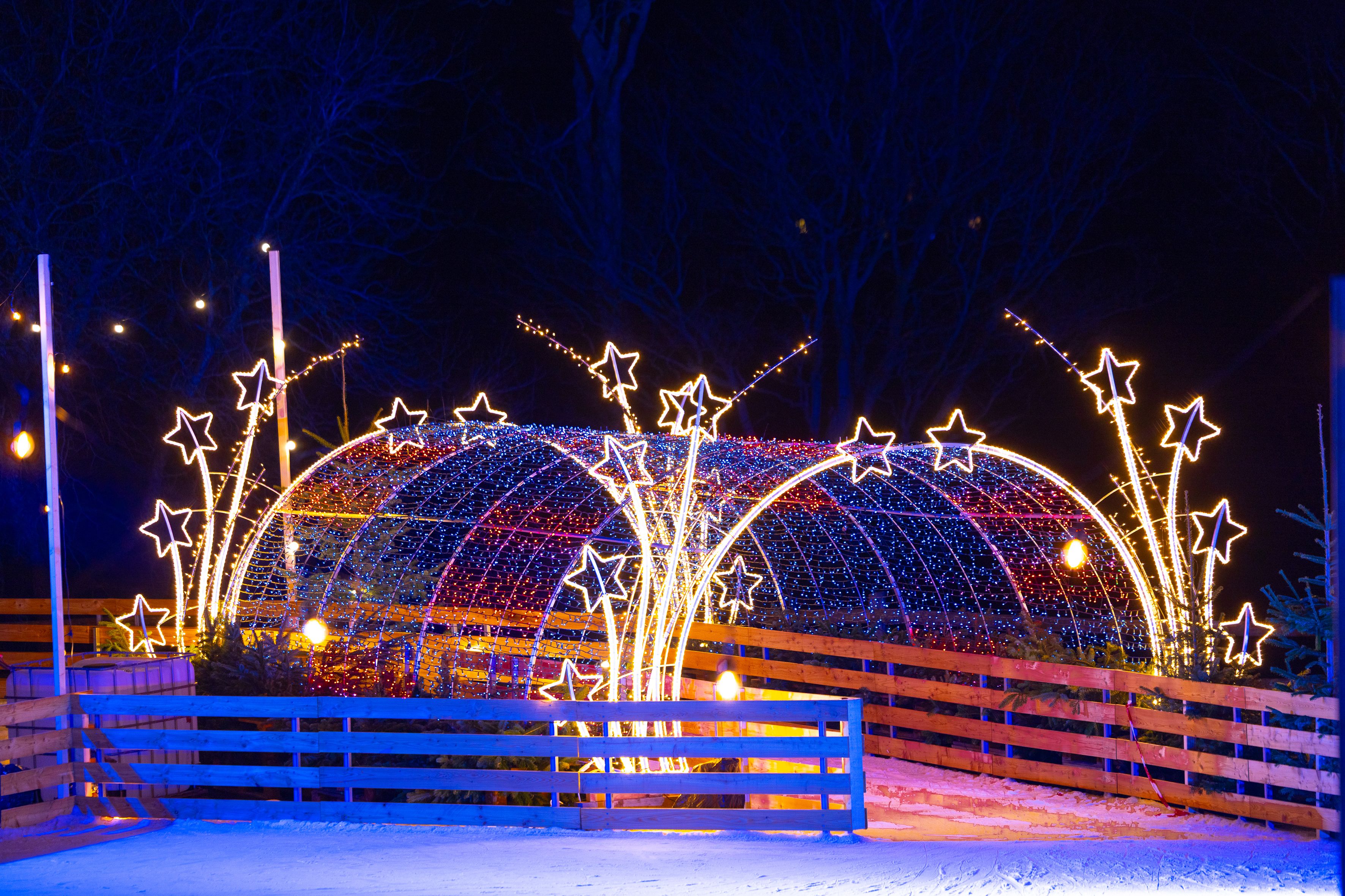 Beleuchteter Eislaufplatz mit Sternen und Lichtertunnel bei Nacht.