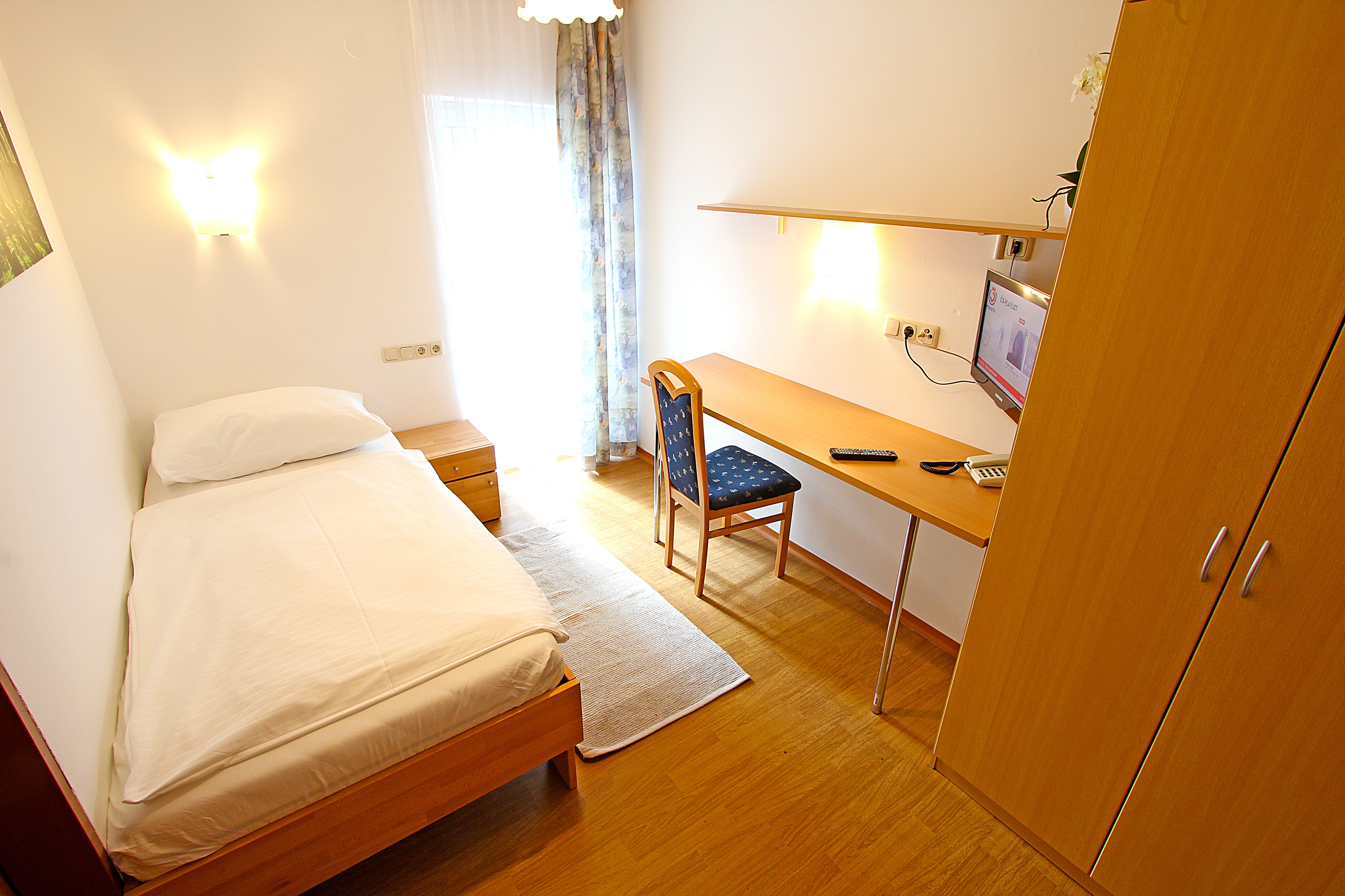 Ein einfach eingerichtetes Einzelzimmer mit Bett, Schreibtisch, Stuhl und Fernseher.