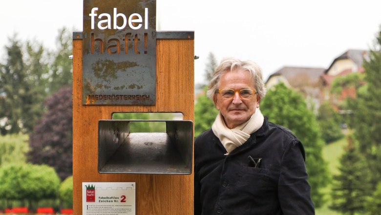 A man stands next to a wooden sign with the words 'fabulous' in a park.