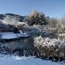Snow-covered garden with pond, bridge and swing in winter.