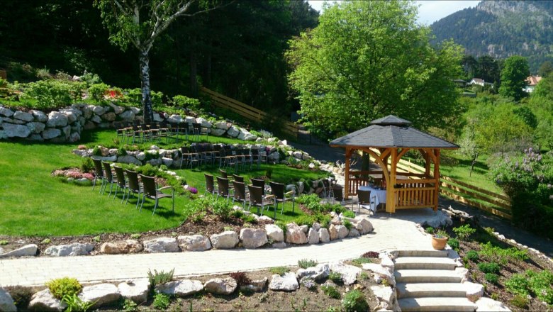 A well-tended garden with a wedding pavilion surrounded by chairs and greenery.