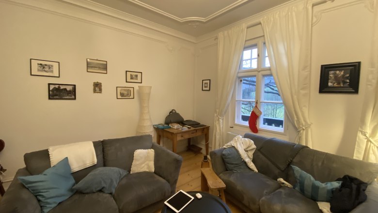 Gemütliches Wohnzimmer mit zwei grauen Sofas, einem runden Tisch, Bildern an der Wand und einem Fenster mit Vorhängen und Weihnachtsstrumpf.