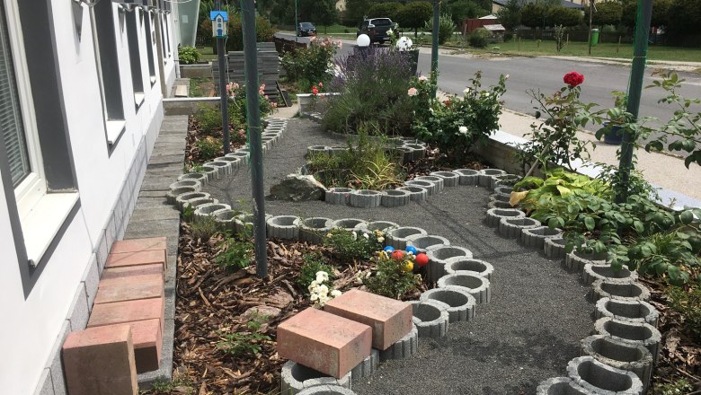 Ein kleiner Garten mit Rosen und einem geschwungenen Weg aus Betonsteinen neben einem Gebäude.