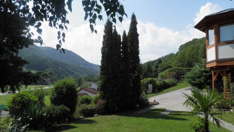 Garten mit Bäumen und Blick auf bewaldete Hügel im Hintergrund.