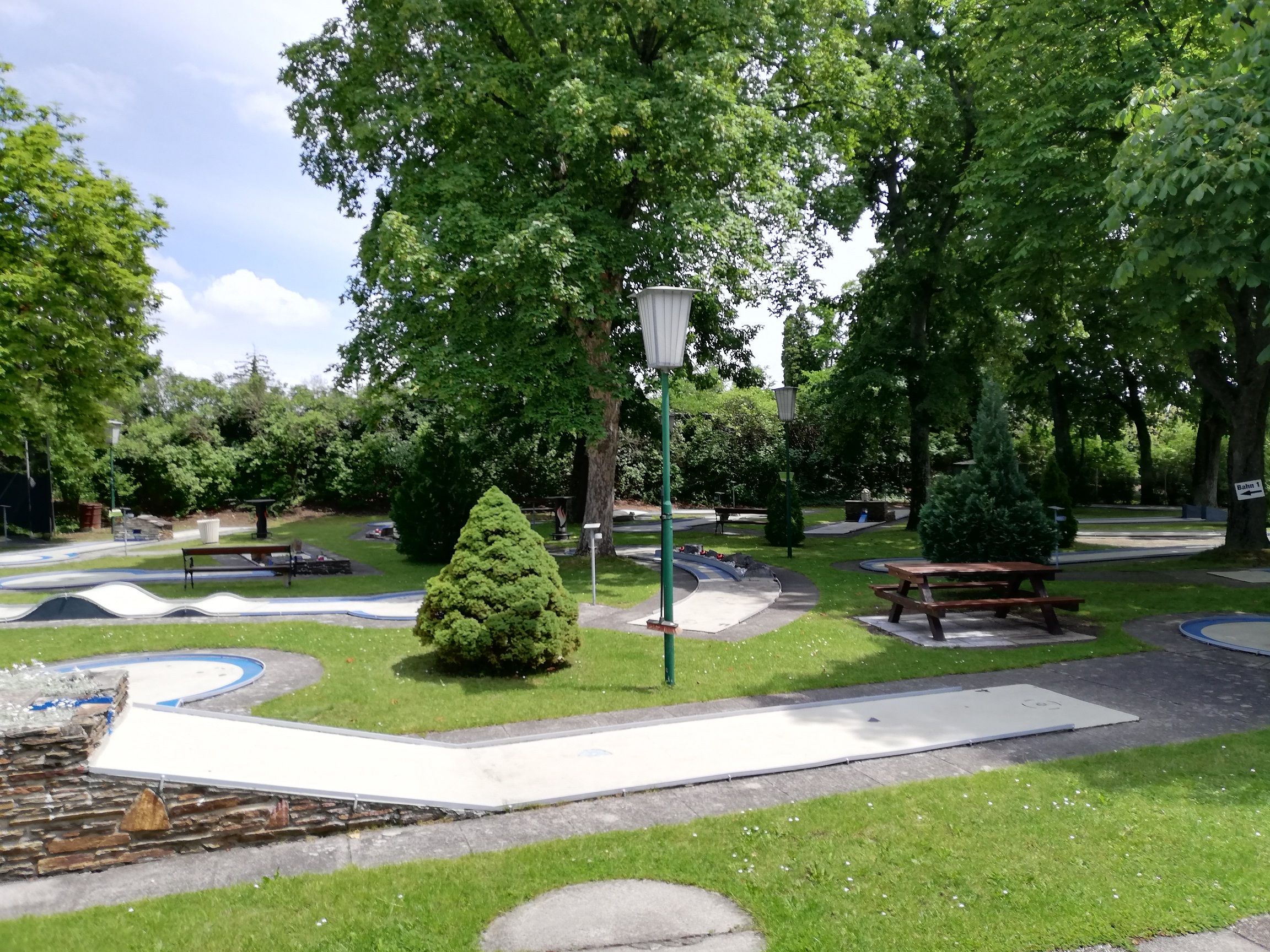 Minigolfplatz mit Bäumen und Bänken in einem Park.