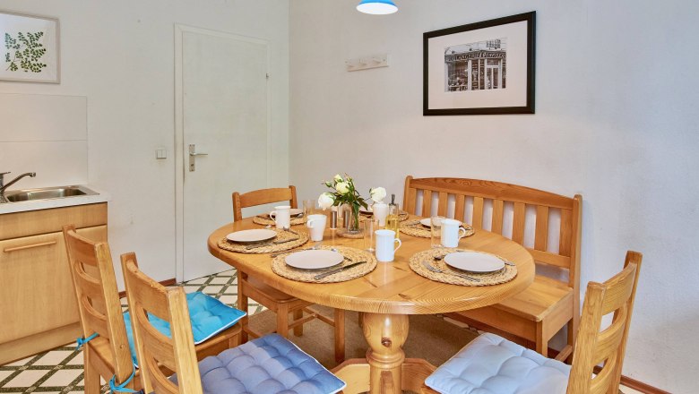 A cozy kitchen table with wooden chairs and blue cushions, set for four people, in a bright room with murals.