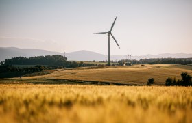 Das Windrad Lichtenegg auf einem Feld, im Hintergrund Berge
