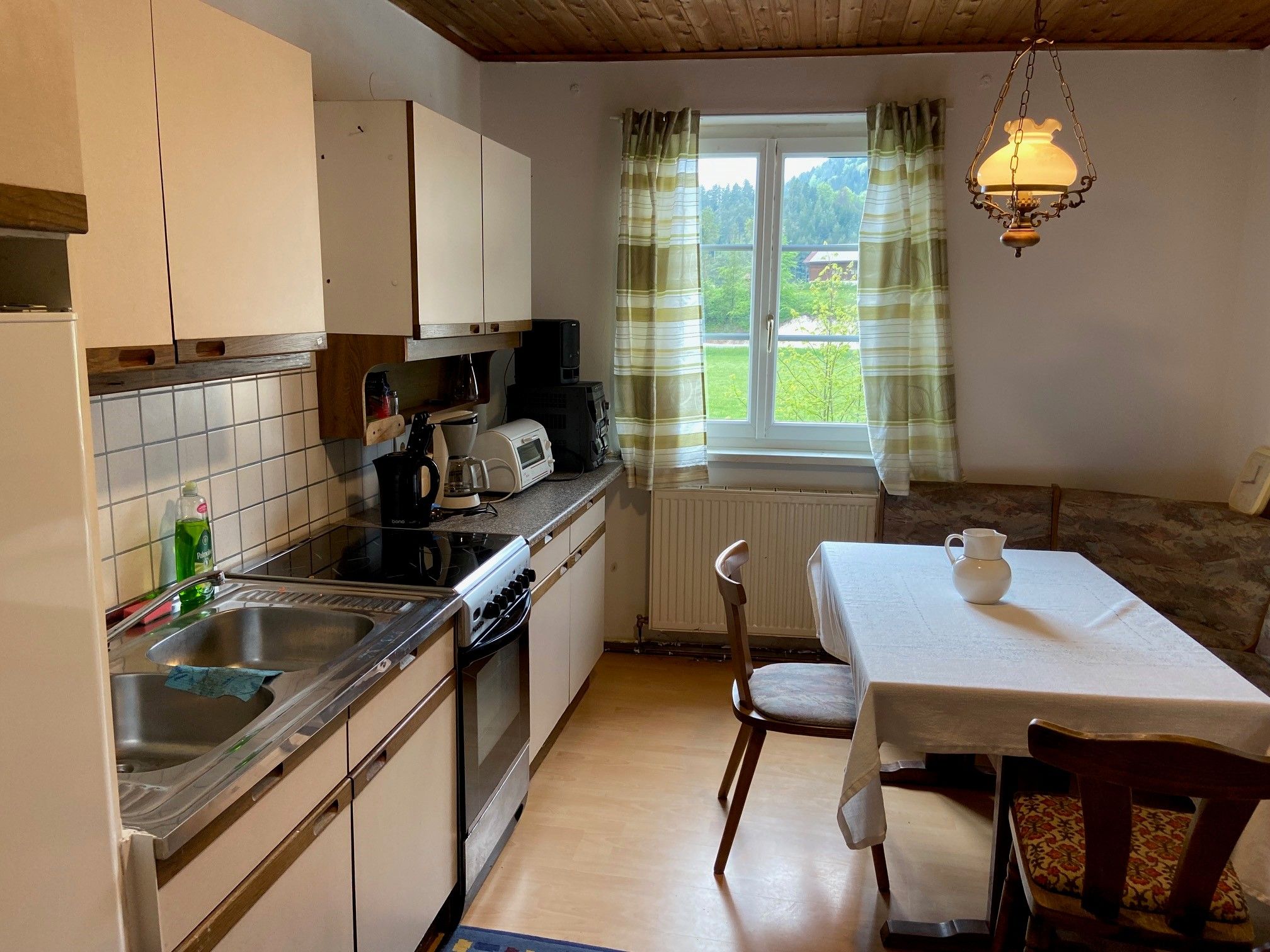 Küche mit Esstisch, Stühlen, Spüle, Herd und Fenster mit Vorhängen.