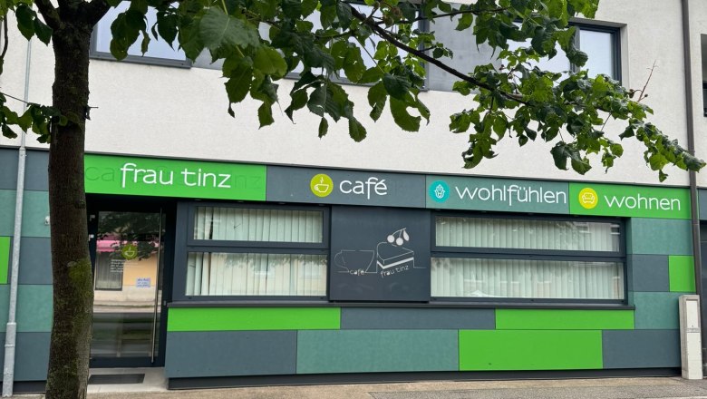 Außenansicht eines Cafés mit grüner Fassade und Baum im Vordergrund.