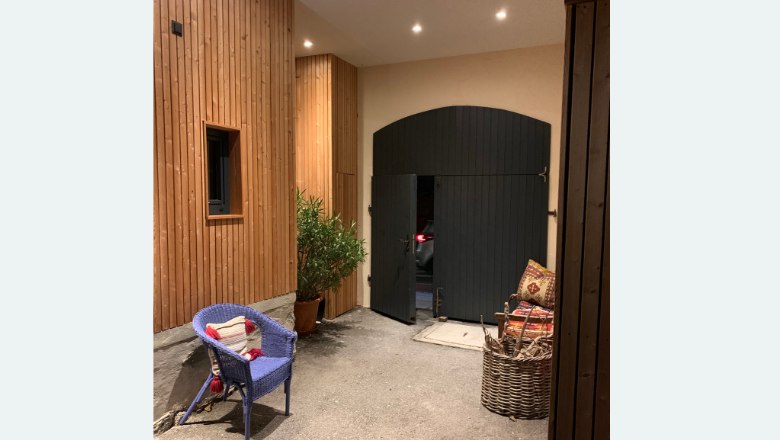 Ein Innenhof mit Holzw&auml;nden, einem blauen Stuhl, einer Pflanze und einem gro&szlig;en schwarzen Tor.