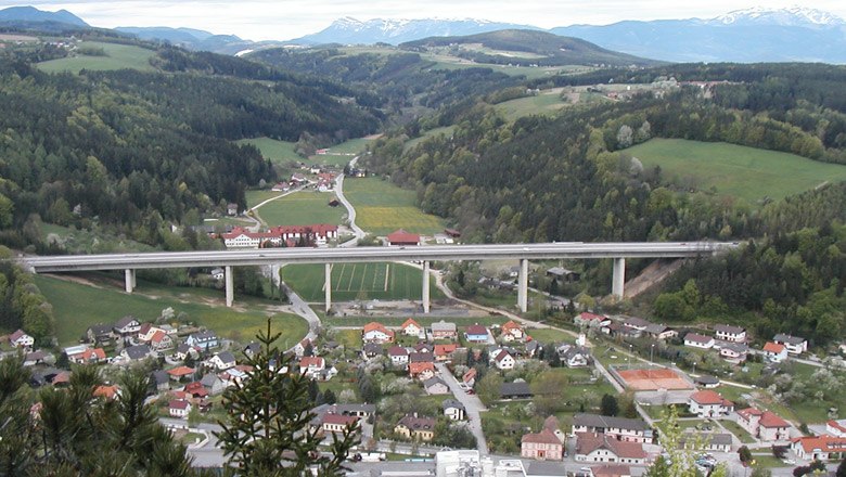 Panoramablick auf die Gemeinde Warth mit Brücke und umliegenden Hügeln.