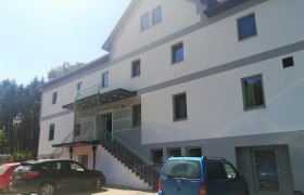 Exterior view of a modern inn with several windows and parked cars in front of it.