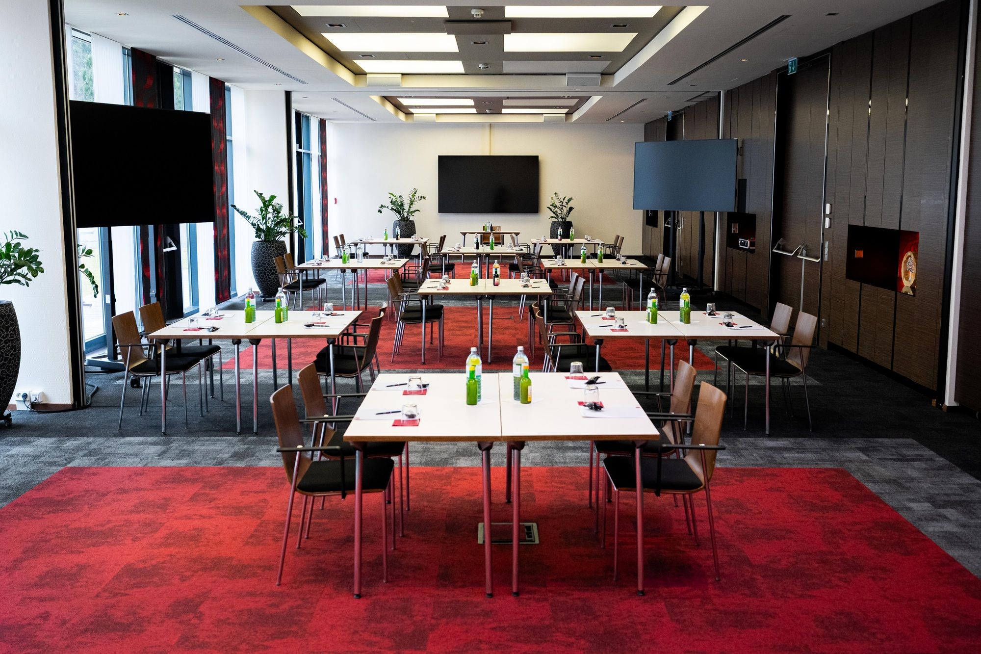 Ein moderner Konferenzraum mit roten Teppichen, weißen Tischen und Stühlen, ausgestattet mit Getränken und Schreibmaterialien.