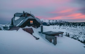In der winterlichen Landschaft erstrahlt das Ottohaus in warmen Farben, w&auml;hrend die schneebedeckten Berge im Hintergrund majest&auml;tisch aufragen. Die ruhige Atmosph&auml;re l&auml;dt dazu ein, die frische Bergluft zu genie&szlig;en und die Sch&ouml;nheit der Wiener Alpen zu erleben.