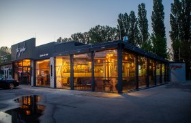 Au&szlig;enansicht eines modernen Restaurants bei D&auml;mmerung mit gro&szlig;en Glasfenstern und warmem Licht.