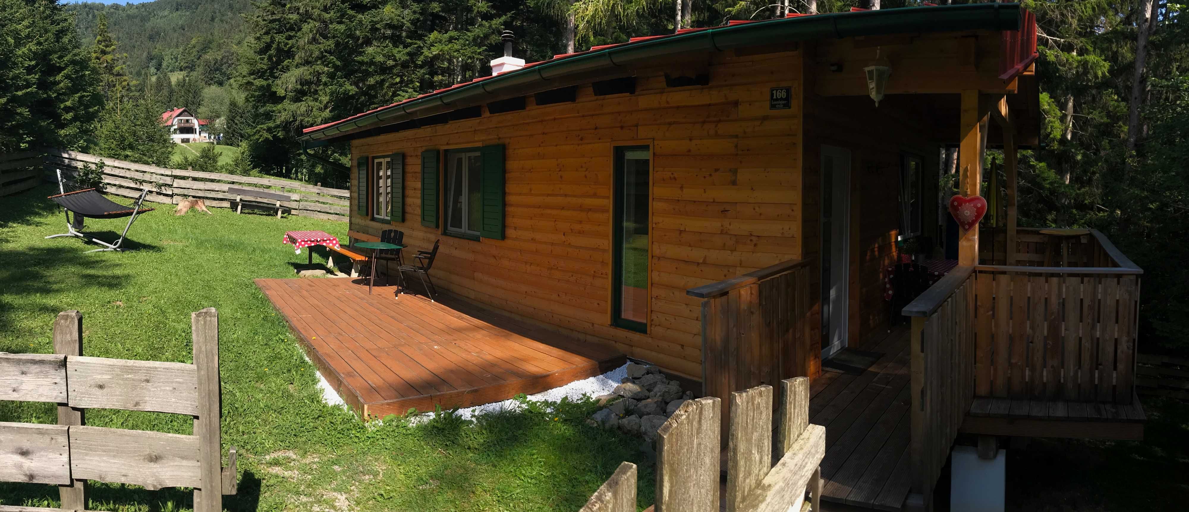 Ein Holzferienhaus mit Terrasse in einer grünen, bewaldeten Umgebung.