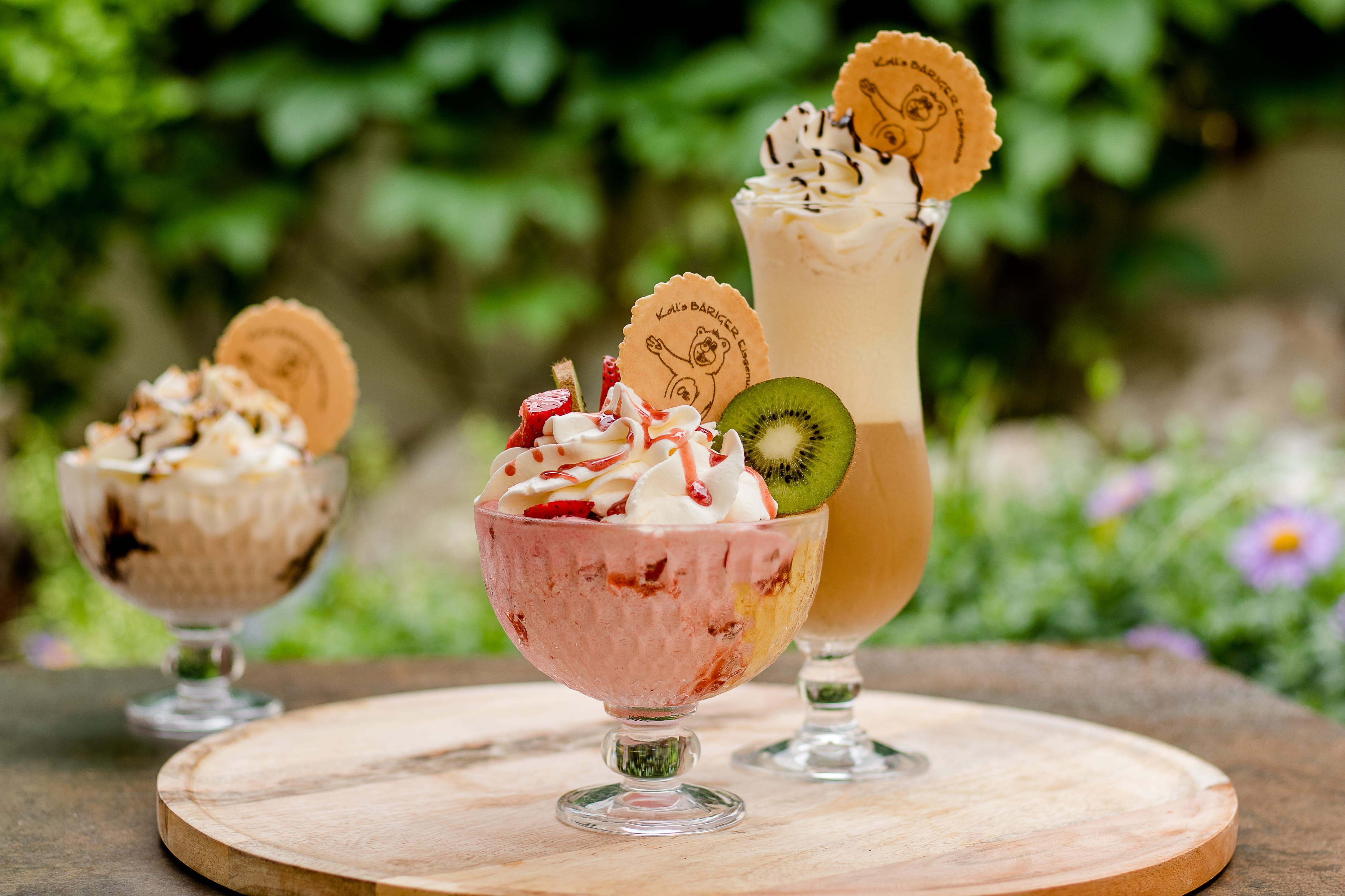 Drei Eisbecher mit Sahne und Dekoration auf einem Tisch im Freien.