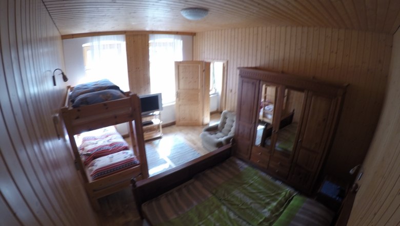 Holzvertäfeltes Schlafzimmer mit Etagenbett, Doppelbett, Kleiderschrank und Fernseher.