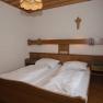 A traditional double room with wooden furniture, two beds, a cross on the wall and a lamp on the ceiling.