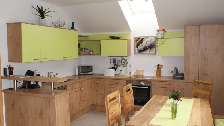 Moderne Küche mit Holzmöbeln und grünen Akzenten, Esstisch mit Vase, Oberlichter.